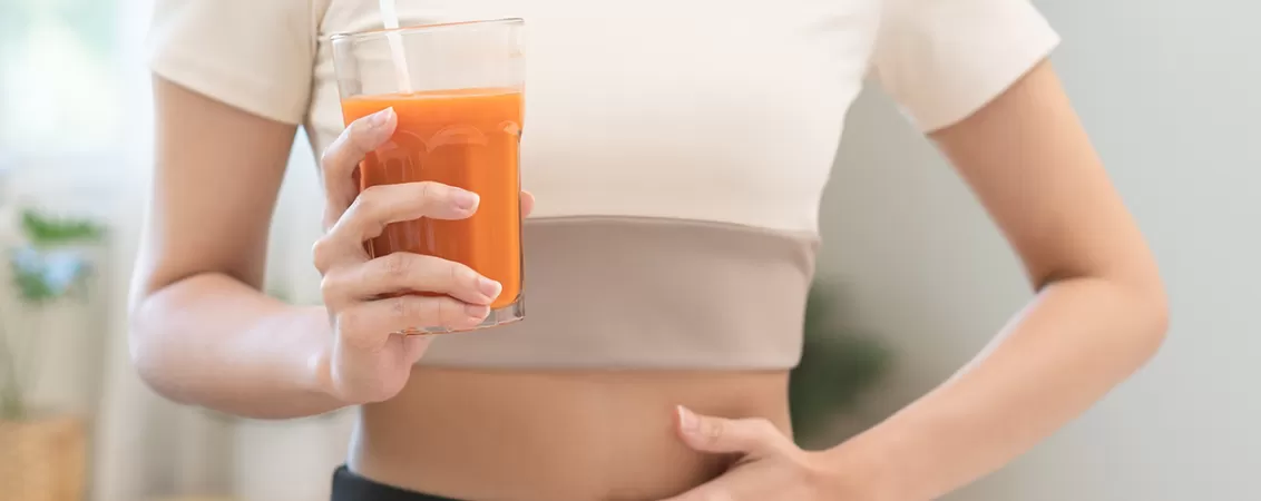 Femeie care bea un pahar de smoothie cu morcovi si alte legume proaspete