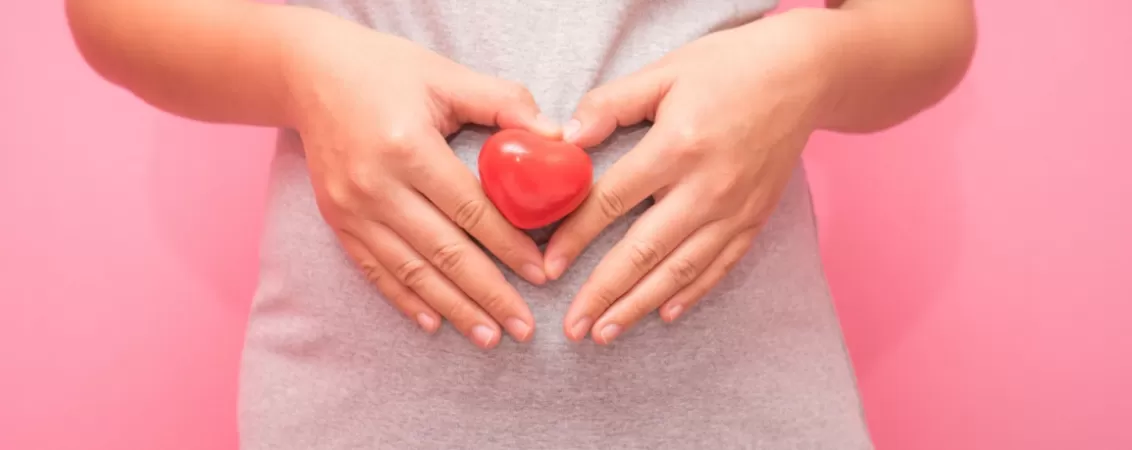 Femeie insarcinata care tine in maini o inima simbolica pe burtica, concept de dragoste maternala si viata noua