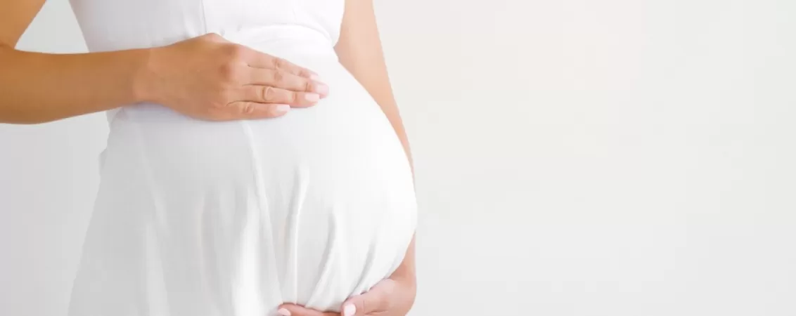 Femeie insarcinata in rochie alba atingandu-si burtica de sarcina avansata