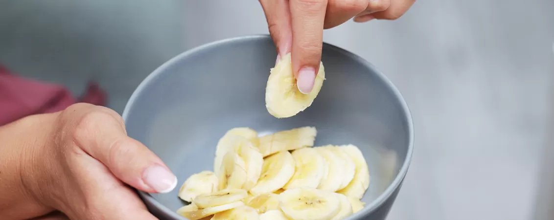 Femeie mancand felii de banana dintr-un bol gri-albastrui