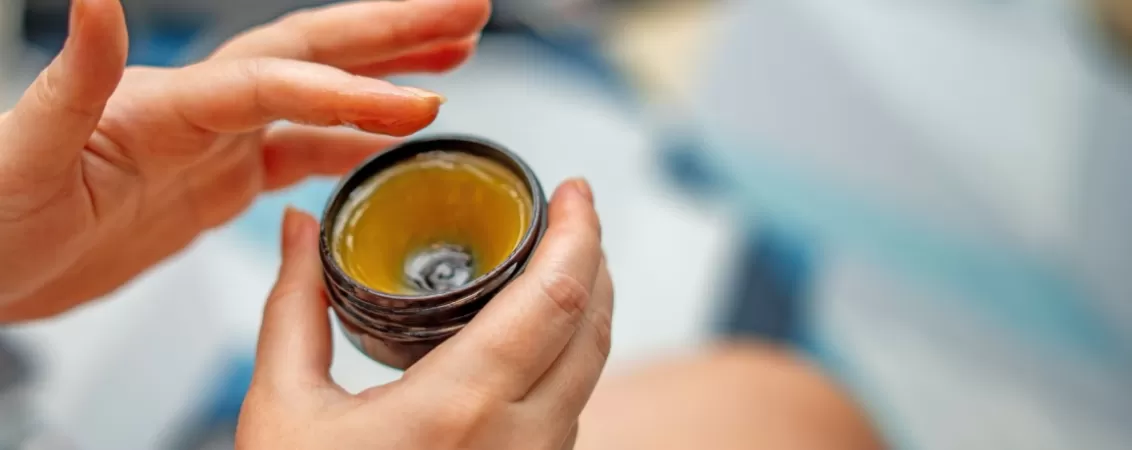 Mainile unei femei aplicand crema cu lanolina dintr-un recipient deschis