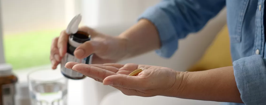 Prim plan al unei femei in varsta cu dementa tinand in palma suplimente cu vitamina E.