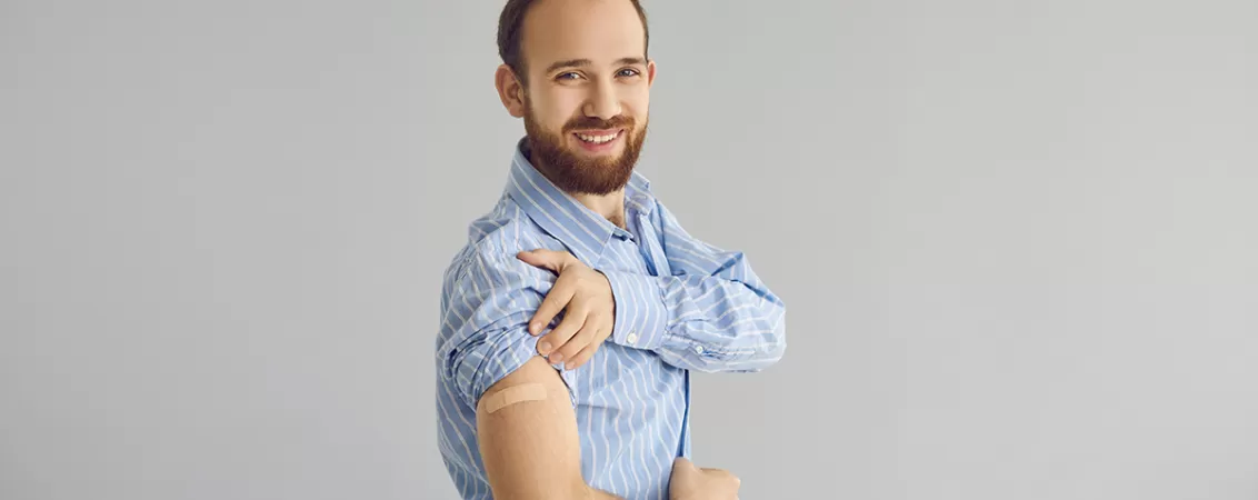 Barbat care zambeste si isi arata umarul cu un mic bandaj, simbol al vaccinarii impotriva HPV la barbati