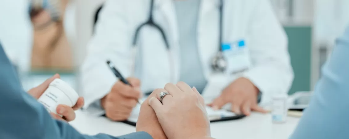 Cuplu care se consulta cu un medic la spital, tinandu-se de mana, in cadrul unei consultatii de fertilitate