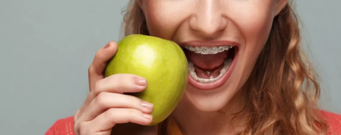 Femeie cu aparat dentar ceramic si cu un mar