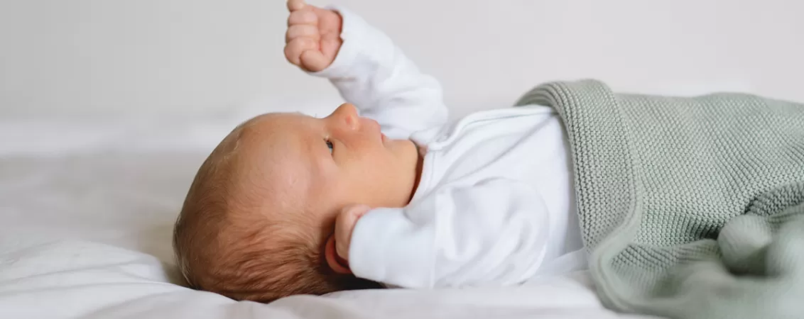 Bebelus nou-nascut intr-un body alb in pat