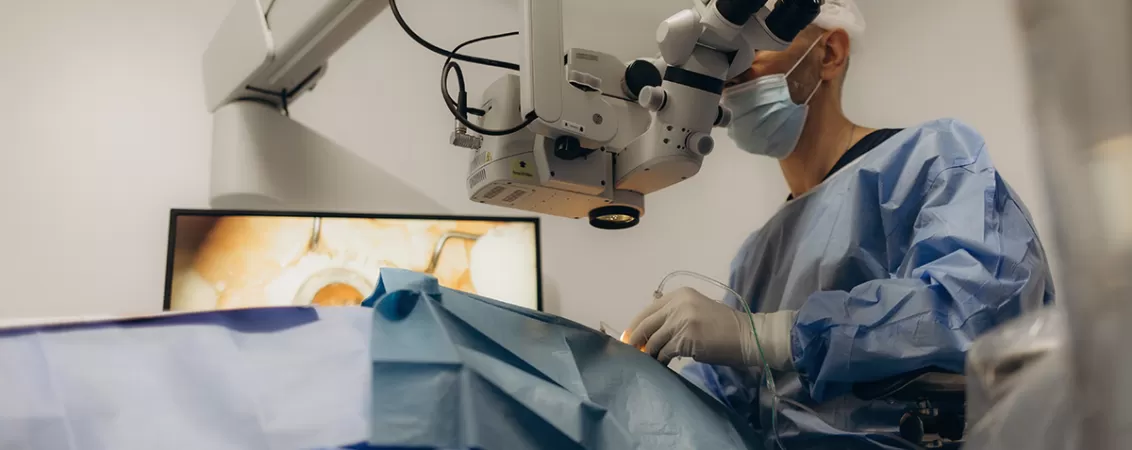 Chirurg care priveste prin microscop in sala de operatie in timpul unei operatii de cataracta