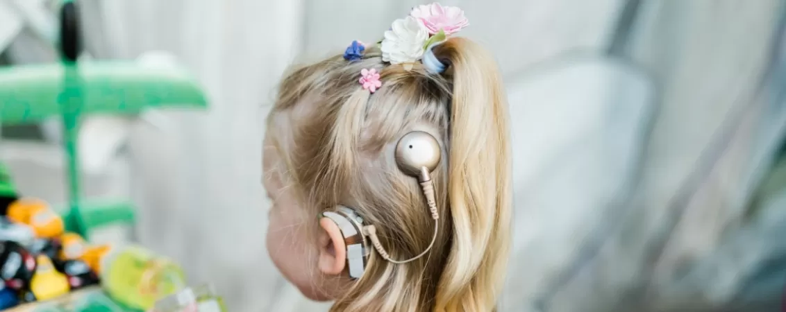 Copil cu spatele, purtand un implant cohlear si un aparat auditiv