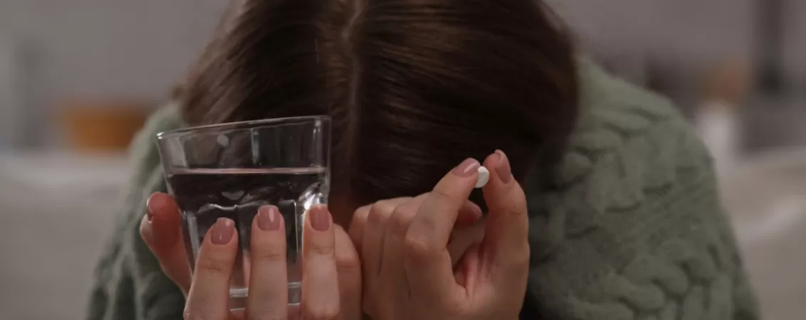 Femeie depresiva tinand o pastila antidepresiva si un pahar cu apa, pregatindu-se sa ia medicamentul