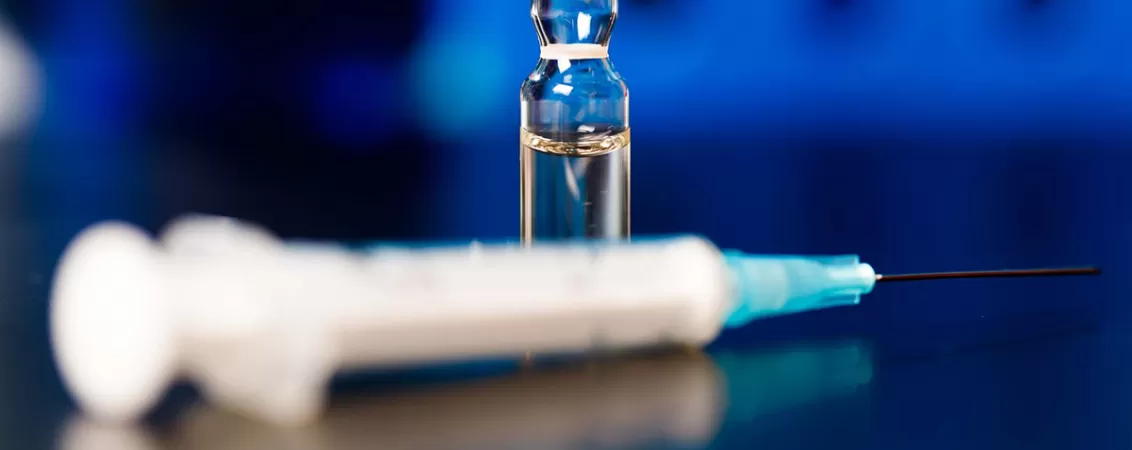 Fiolă cu medicament de terapie genică și seringă pe un fundal albastru închis.