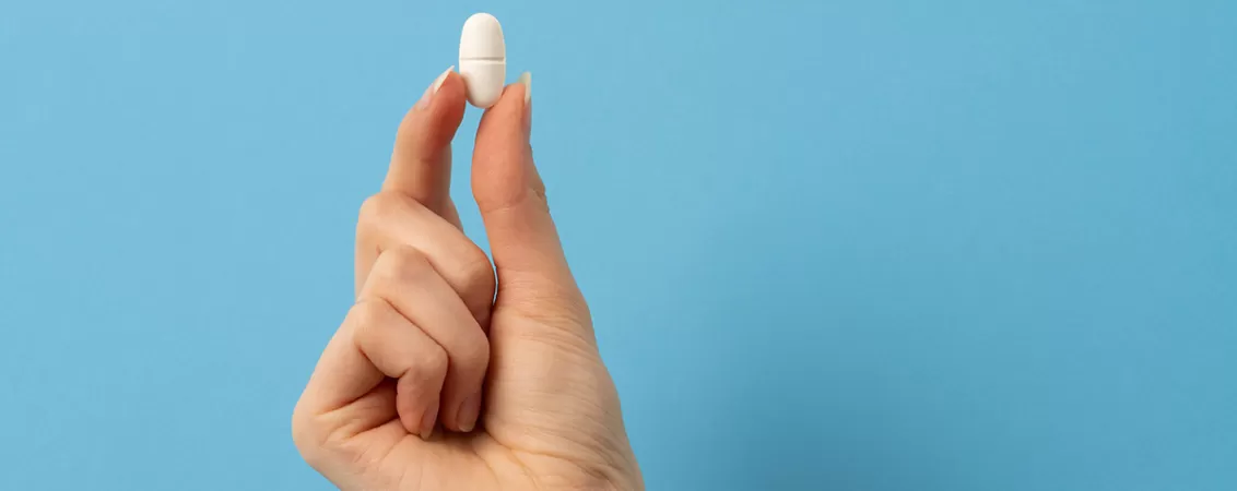 Mana unei femei care tine o singura pastila pe fundal albastru deschis, concept de tratament individual