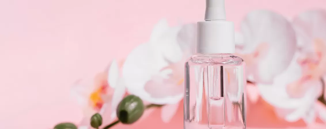 Sticla transparenta cu pipeta care contine ser cosmetic cu panthenol pe fundal roz pastel