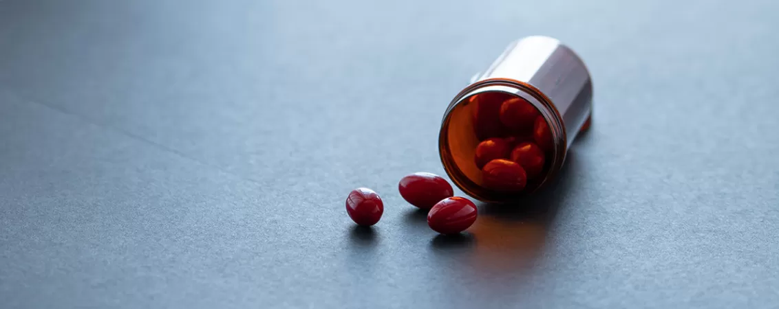 Capsule rosii langa o sticla de plastic maro, concept de medicamente sau suplimente