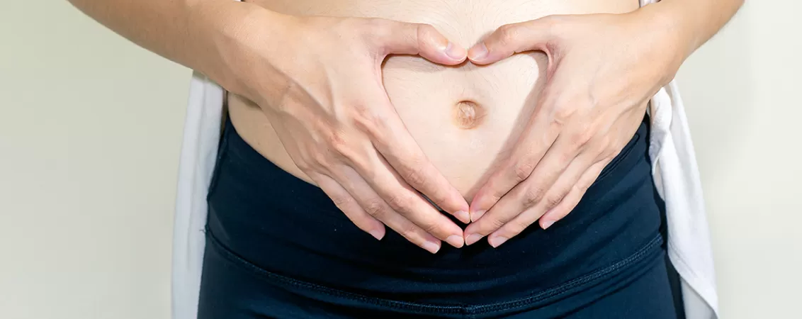 Femeie insarcinata care sta in picioare si isi atinge usor burtica, expresie de grija si afectiune