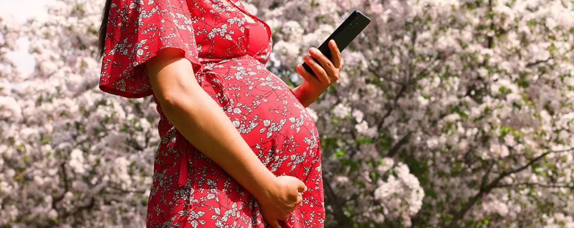 Femeie insarcinata folosind o aplicatie pe telefon in timp ce citeste informatii despre sarcina