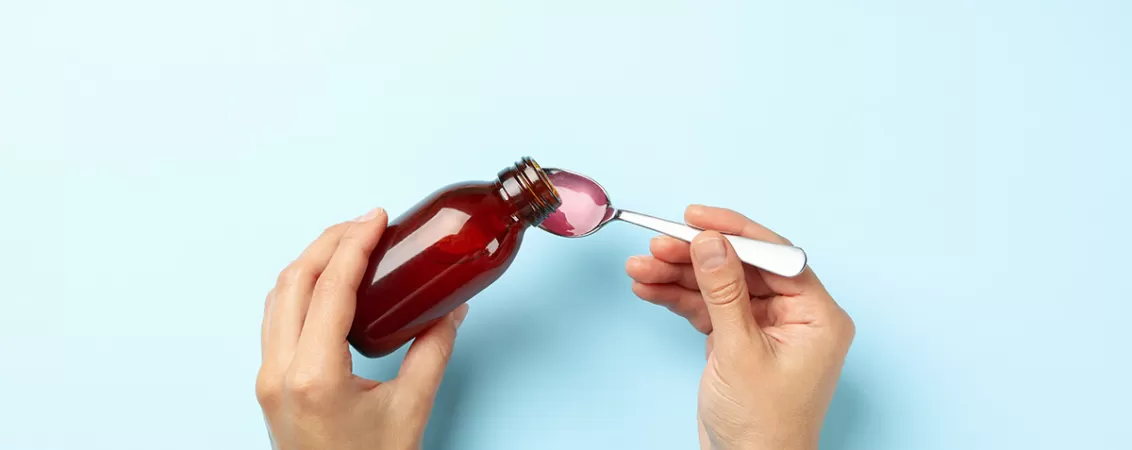 Femeie turnand sirop de medicament pe o lingurita, pe fundal albastru