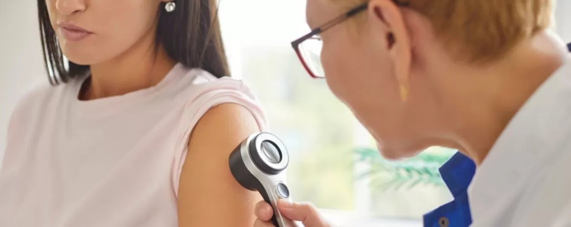 Medic dermatolog examinand pielea unei femei in timpul unui consult dermatologic