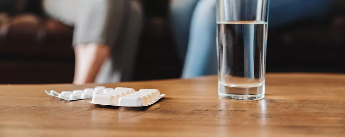 Prim-plan cu un pahar cu apa curata si pastile, simbol al administrarii medicamentelor