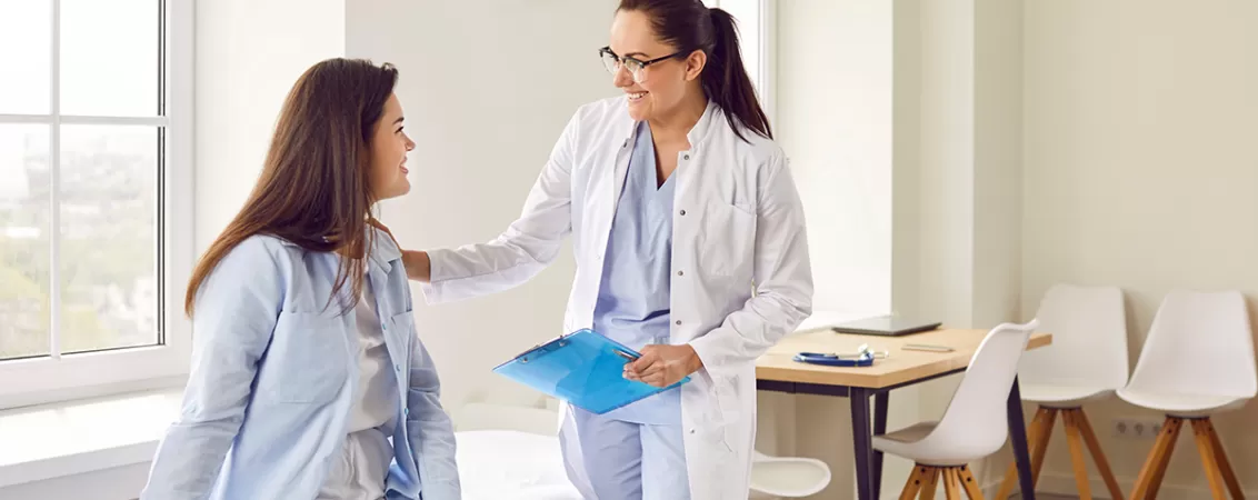 Tanara femeie insarcinata zambitoare care discuta cu medicul sau in timpul unei consultatii prenatale