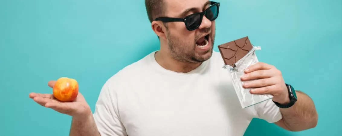 Barbat care tine intr-o mana o ciocolata si intr-o mana un fruct