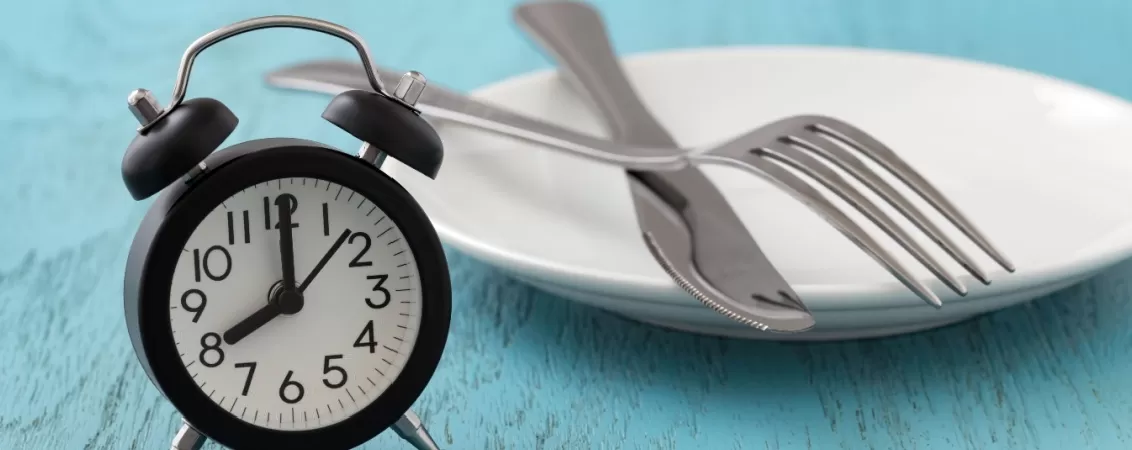 Ceas desteptator care arata ora 8 langa o farfurie goala