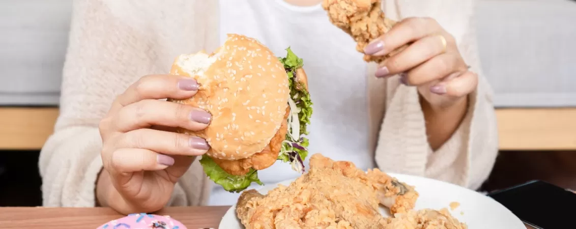 Femeie care mananca hamburger crispy si gogoasa in acelasi timp