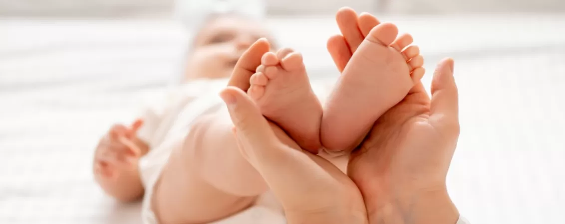 Mainile unei femei tinand piciorusele unei fetite de cateva luni