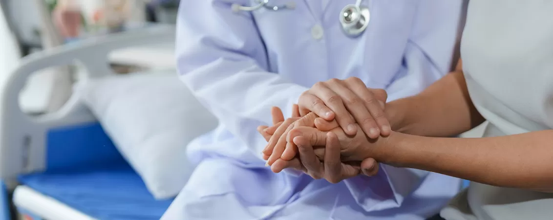 Medic tinand mainile unei paciente pe patul de spital