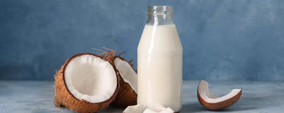 Sticla cu lapte de cocos langa nuci cocos sparte in jumatate