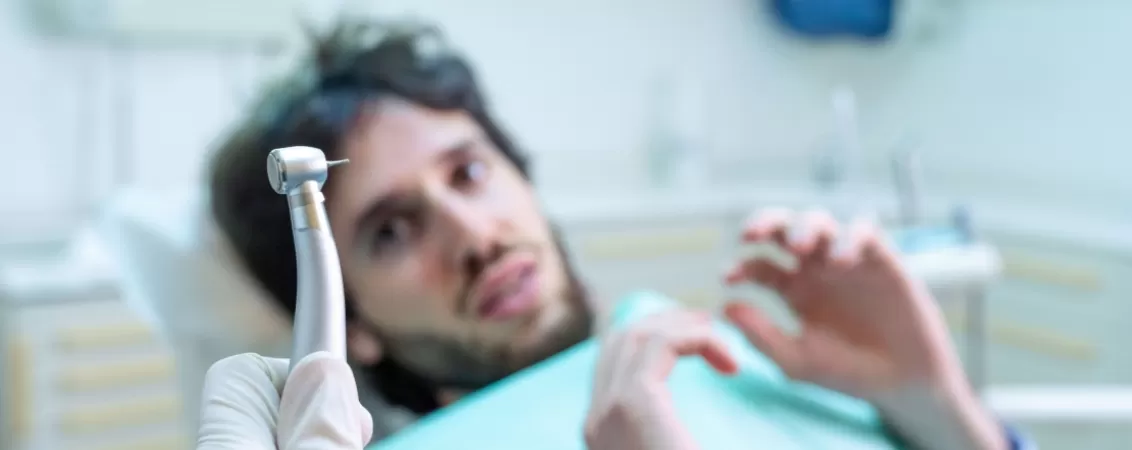 Barbat care se teme de freza tinuta in mana de un dentist