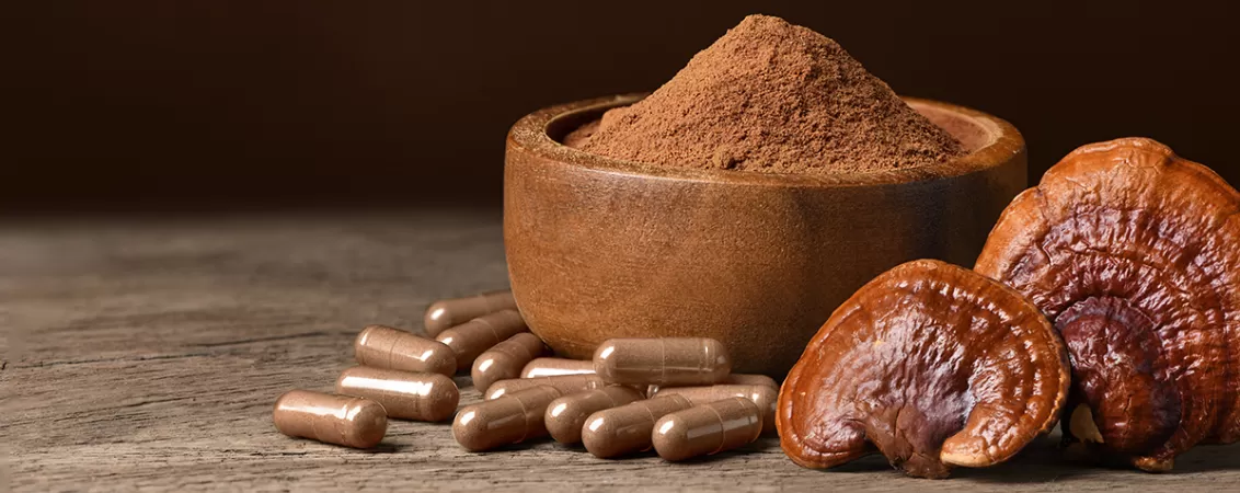 Capsule si pulbere de ciuperca reishi lingzhi pe o farfurie de lemn, prezentand supliment natural pentru sanatate