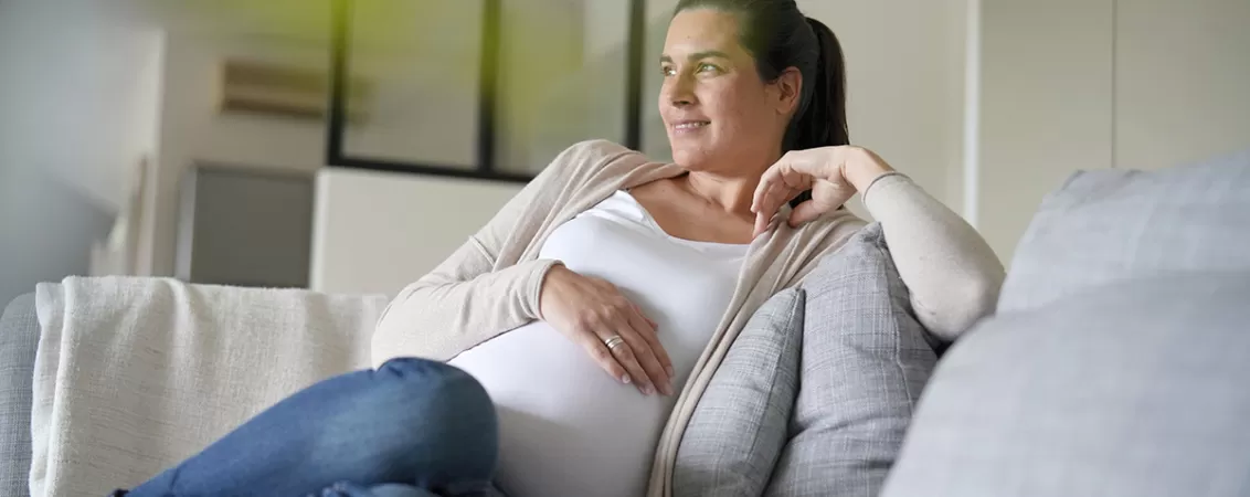 Femeie insarcinata care se relaxeaza pe canapea, exprimand stare de bine si confort in timpul sarcinii