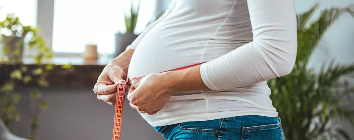 Femeie insarcinata isi masoara burtica cu banda de masurat, urmarind evolutia sarcinii si schimbarile corporale