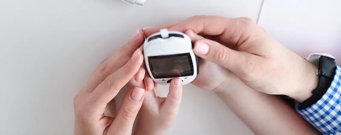 Mainile mamei si ale fiicei tinand un glucometru, evidentiind monitorizarea glicemiei acasa si educatia privind diabetul