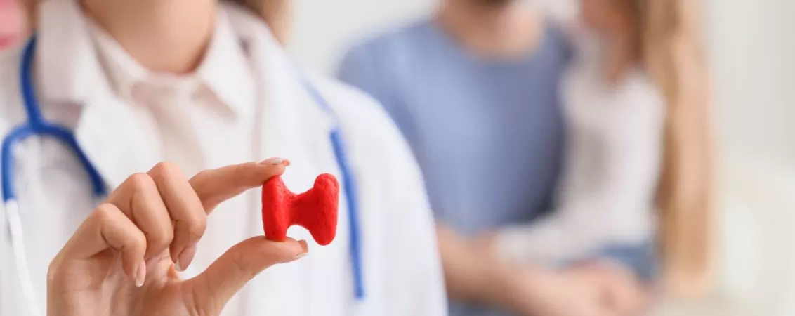 Medic endocrinolog in cabinet cu modelul glandei tiroide si pacienti pe fundal