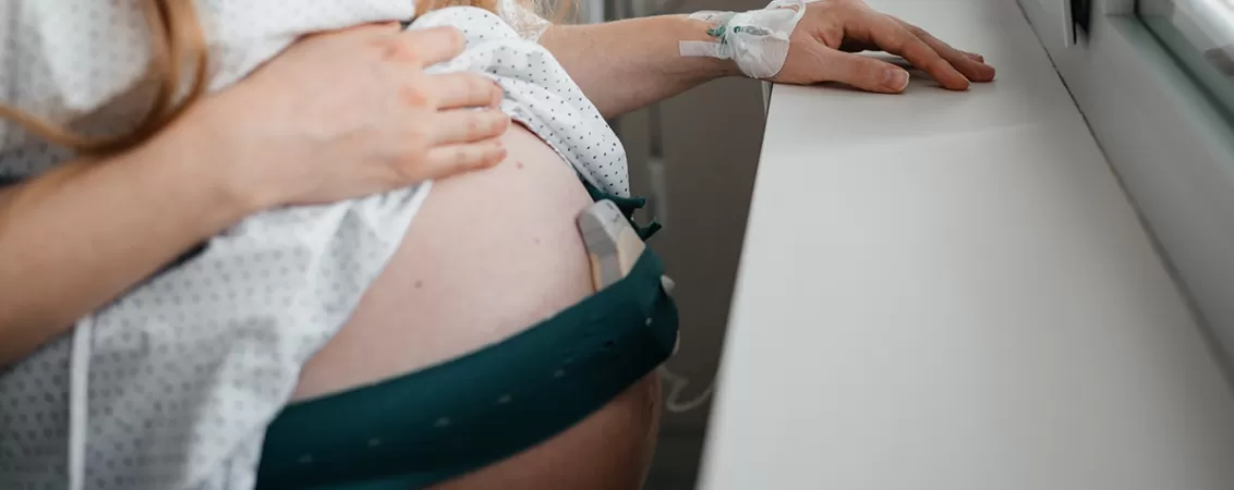 Prim plan cu femeie insarcinata in halat de spital cu perfuzie, sugerand monitorizarea medicala in perioada prenatala