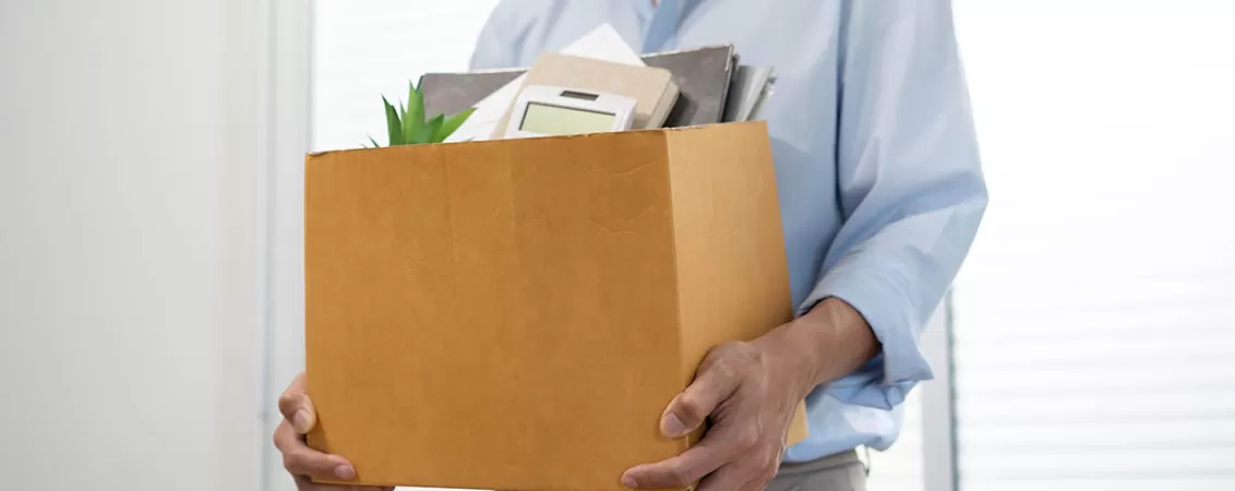 Barbat care tine in maini o cutie cu lucrurile personale, pentru a elibera spatiul de lucru dupa ce si-a dat demisia, ilustrand procesul de plecare de la locul de munca si tranzitia profesionala.