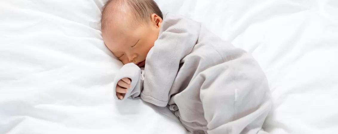 Bebelus asiatic nou nascut care doarme linistit, sugerand stare de confort, siguranta si sanatate in primele zile de viata