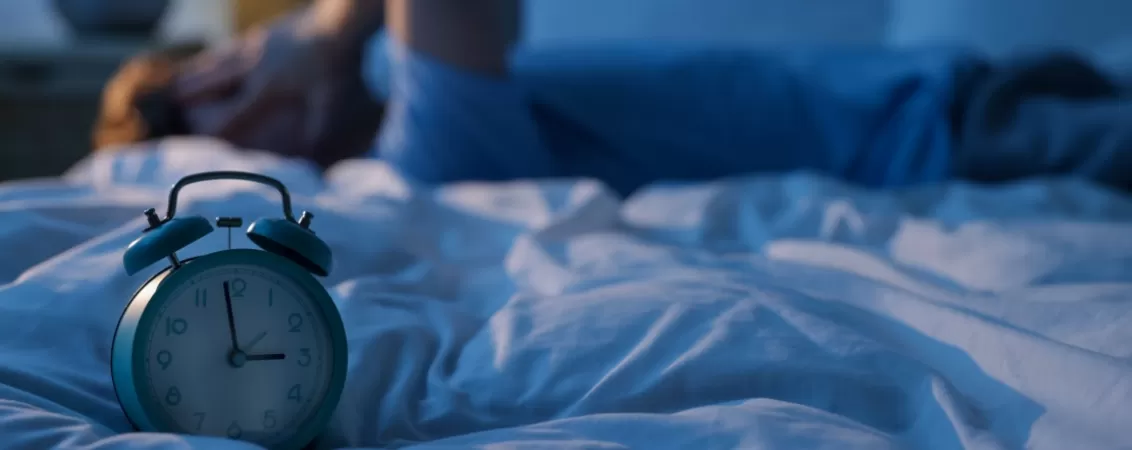 Ceas care arata ora 3 noaptea si un barbat care nu poate adormi