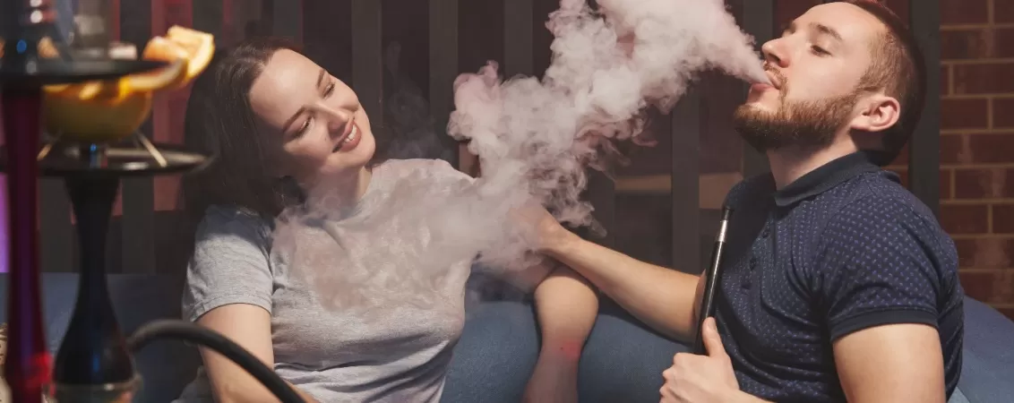 Cuplu in care ea il priveste pe el fumand narghilea