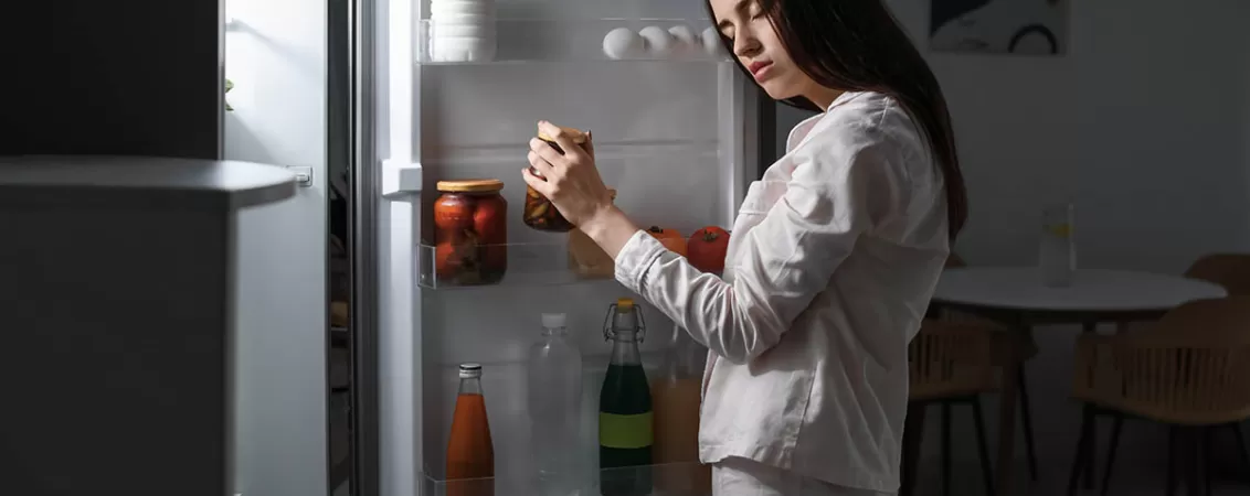 Femeie somnambula apropiindu-se de frigider noaptea, in intuneric, ilustrand actiunile involuntare in timpul somnambulismului si rutina nocturna neconstienta.