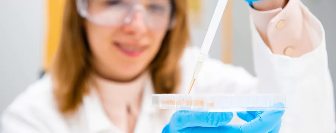 Tanara chimista purtand ochelari de protectie si manusi din cauciuc, lucrand in laborator pentru analize si cercetare stiintifica