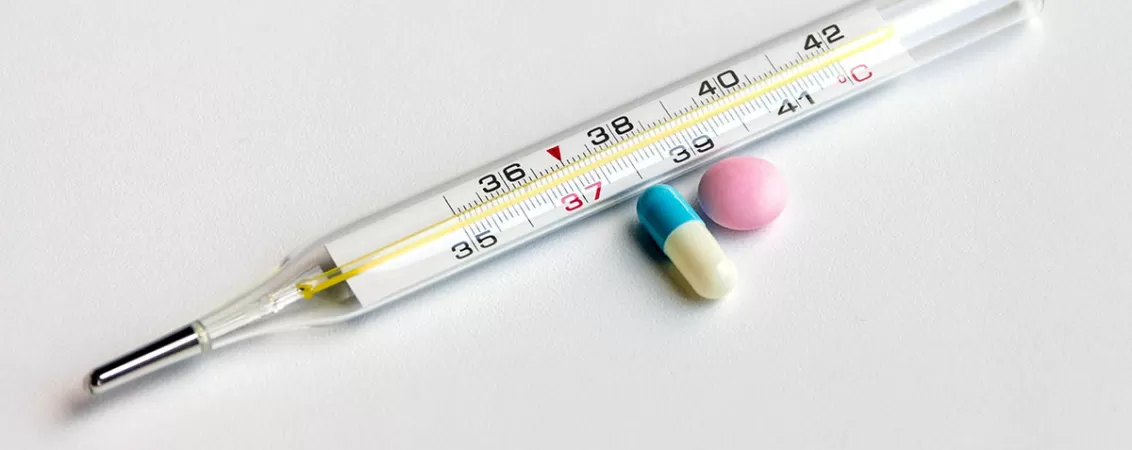 Termometru medical alaturi de pastila antipiretica, ilustrand masurarea temperaturii si tratamentul simptomatic pentru febra.