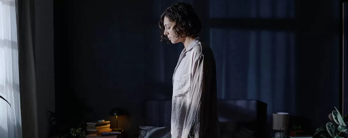 Vedere laterala a unei femei care sufera de somnambulism, mergand printr-o incapere intunecata in timp ce doarme.