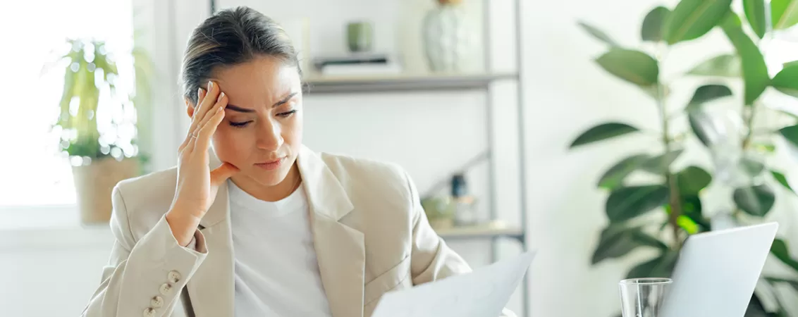 Femeie analizand niste acte, incruntata si stresata, ilustrand presiunea profesionala si starile emotionale negative asociate suprasolicitarii.