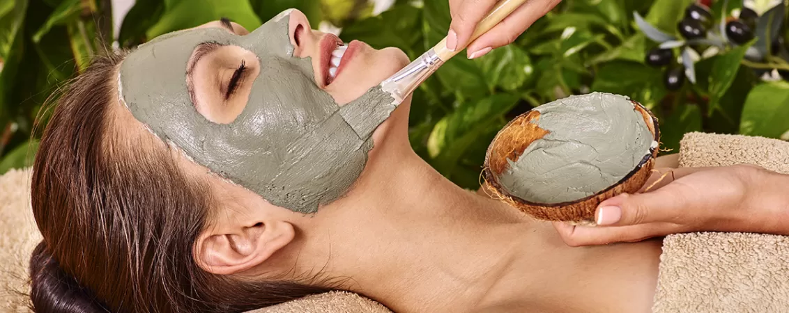 Femeie aplicand masca faciala cu argila in timpul unui tratament de infrumusetare, evidentiind rutina de ingrijire a pielii si beneficiile detoxifierii tenului.