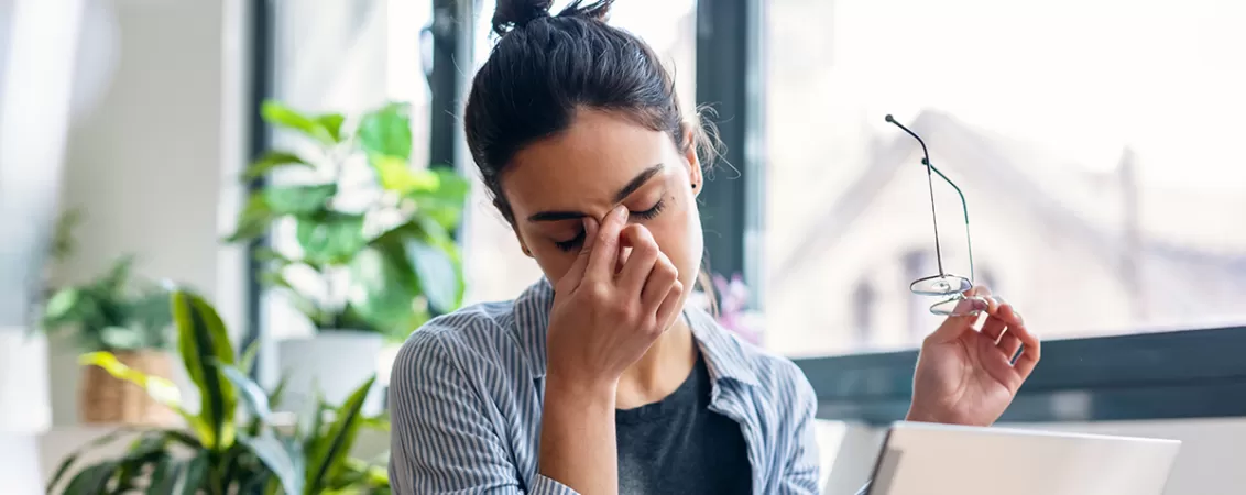 Femeie de afaceri stresata lucrand de acasa, aratand oboseala mentala, reprezentand presiunea muncii si lipsa concentrarii care apare in cazul suprasolicitarii la locul de munca