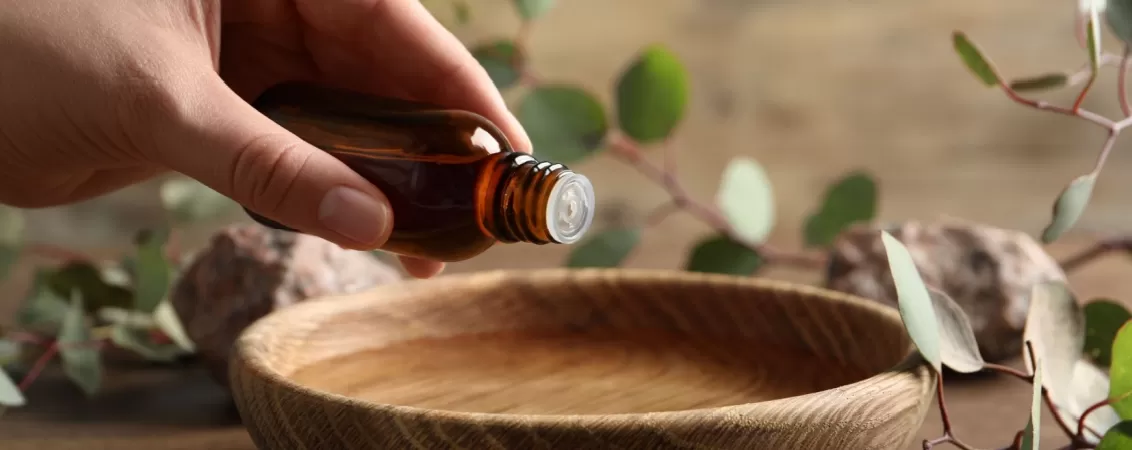 Femeie adaugand ulei de eucalipt intr-un bol cu apa