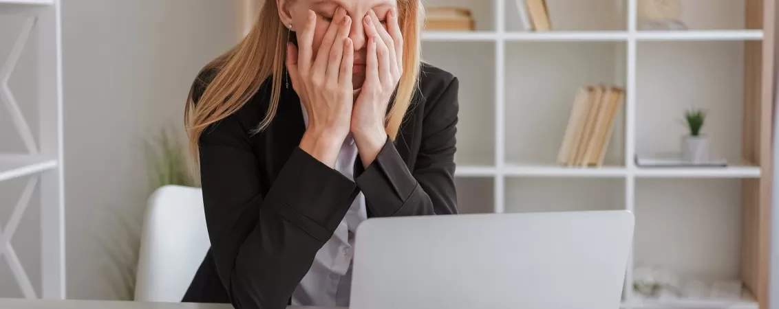 Angajat lucrand intens la laptop cu suprasolicitare informationala si oboseala oculara in birou modern