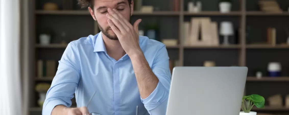 Barbat care lucreaza la biroul de acasa si care a luat o pauza de la privitul la laptop pentru a-si relaxa ochii obositi